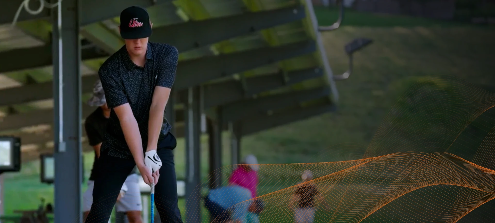 Person in a black cap and shirt preparing to swing a golf club at a driving range, with others practicing in the background.