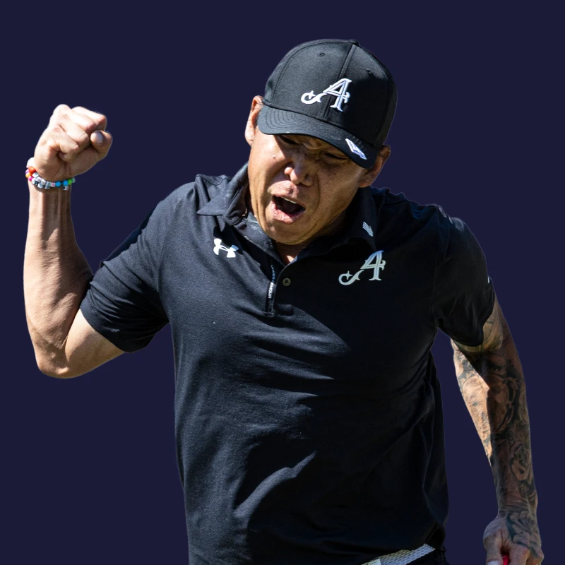 A man in a black sports outfit and cap pumps his fist in celebration against a dark background.