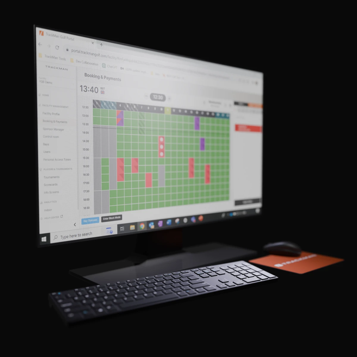 A computer screen displays a booking and payment grid interface, with a keyboard and mouse on the desk below.