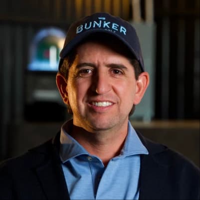 Man wearing a "BUNKER" cap, smiling, in a dimly lit setting with blurred background.